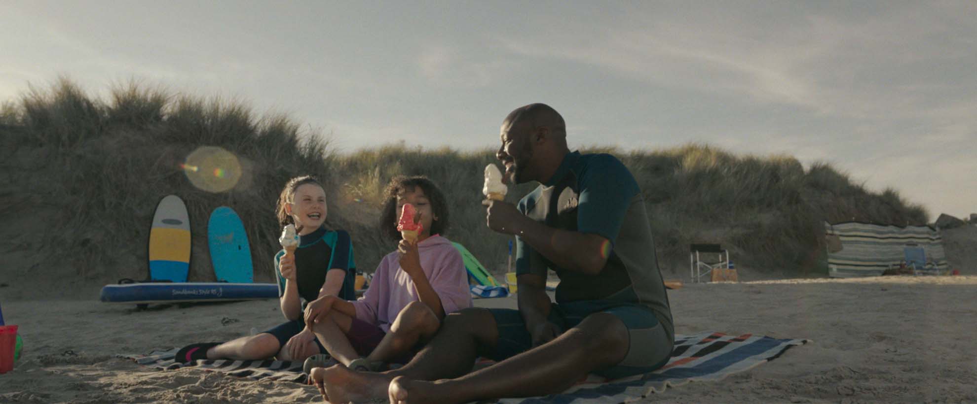Still from VisitBritain film of family of three sitting on beach eating ice-cream