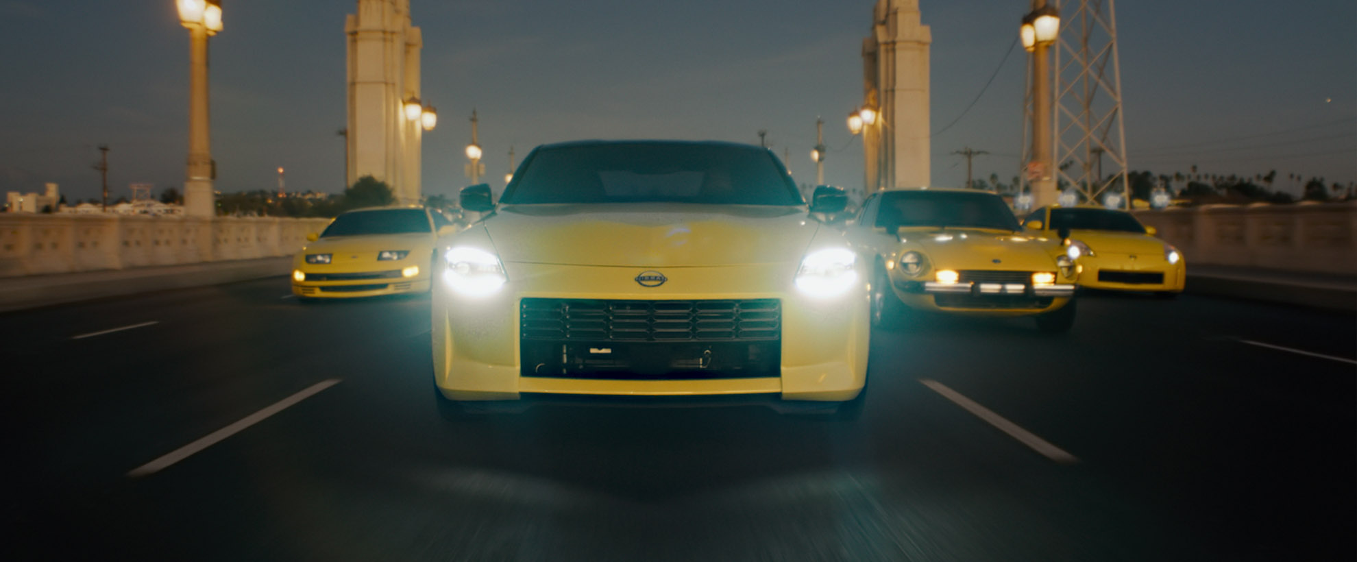 Four yellow Nissan Z vehicles drive across a bridge - each a different variation of the model