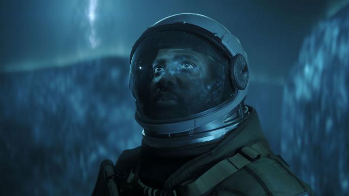 A person in a spacesuit stands in front of a neon blue extraterrestrial-like CGI gaseous wall with an alien entity's silhouette looming  