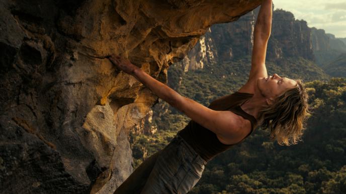 A still from Apex showing Sasha (played by Charlize Theron) climbing a rock face high above an Australian gorge