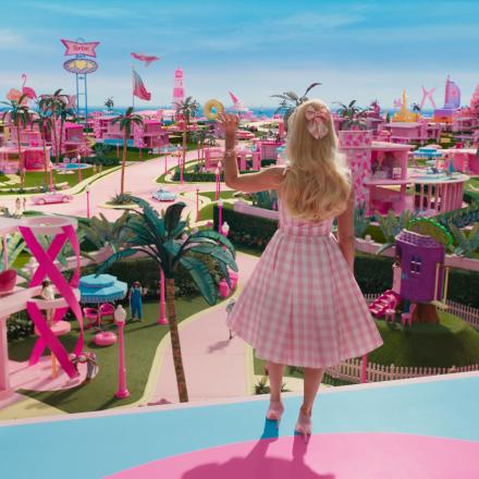 A still of Barbie looking out over a photoreal CGI Barbieland waving. 